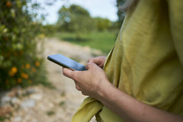 Frau, die mit ihrem Smartphone im Garten SMS schreibt - ANNF00249