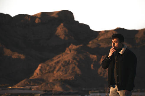 Junger Mann raucht in der Nähe von Bergen bei Sonnenuntergang - DMHF00002