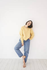 Smiling woman in casual clothes leaning on white wall - EYAF02660