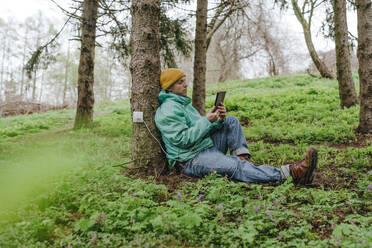 Mann mit Tablet-PC, verbunden mit einer Steckdose auf einem Baum im Wald - YTF00763