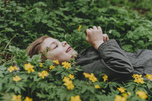 Happy girl lying by yellow flowers in forest - YTF00781