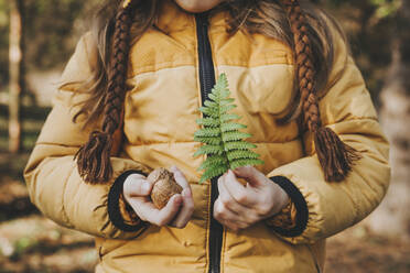 Mädchen hält Nüsse und Farn im Wald - YTF00789