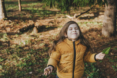 Playful girl holding nuts and fern in forest - YTF00790