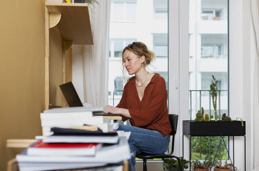 Freelancer working on laptop at desk in home office - MIKF00244