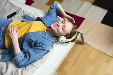 Young woman enjoying music with headphones lying on bed - MIKF00278