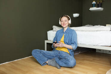 Glückliche junge Frau, die mit Kopfhörern auf dem Boden sitzend Musik genießt - MIKF00283