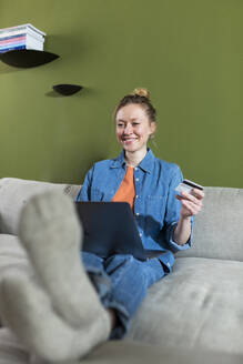 Glückliche junge Frau beim Online-Shopping mit Kreditkarte zu Hause - MIKF00288