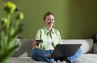 Glückliche Frau beim Homeshopping mit Laptop auf der Couch - MIKF00293