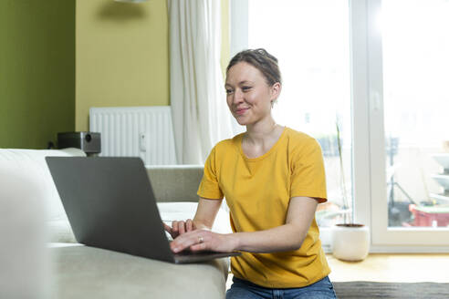 Freiberufler in gelbem T-Shirt bei der Arbeit mit Laptop zu Hause - MIKF00295
