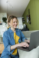 Freelancer in denim shirt working with laptop on couch - MIKF00301