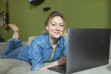 Freelancer in denim shirt working with laptop lying on couch - MIKF00304