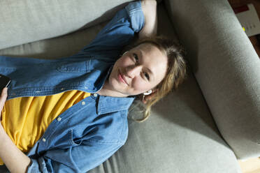 Frau genießt Musik mit drahtlosen In-Ear-Kopfhörern auf der Couch liegend - MIKF00308