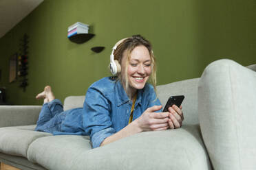 Glückliche junge Frau führt einen Videoanruf mit einem Smartphone auf der Couch - MIKF00311
