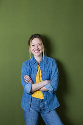 Happy woman with arms crossed in front of green wall - MIKF00320