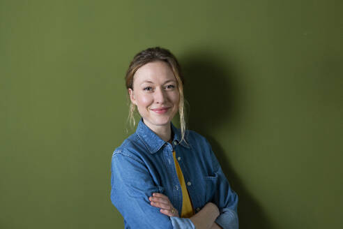 Young woman smiling in front of green wall - MIKF00323