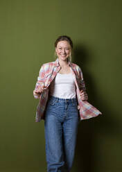Lächelnde junge Frau in kariertem Hemd vor einer grünen Wand stehend - MIKF00330