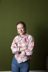 Confident woman with arms crossed in front of green wall - MIKF00335