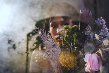 Frau mit Blumenstrauß hinter Glaswand - YTF00797