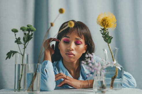 Frau sitzt am Tisch mit Blumen vor blauem Hintergrund - YTF00799