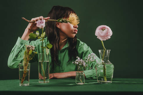 Woman hiding face with Leucospermum at table in front of green backdrop - YTF00813