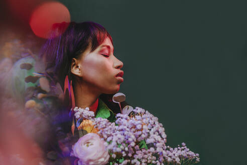 Frau mit geschlossenen Augen inmitten von Blumen und Neonlichtern vor einem grünen Hintergrund - YTF00821