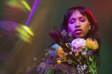 Woman with eyes closed amidst colorful flowers and neon lights - YTF00823