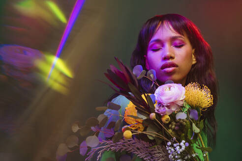 Frau mit geschlossenen Augen inmitten von bunten Blumen und Neonlichtern - YTF00823