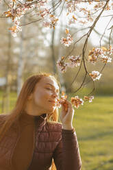 Woman smelling flowers on branch at park - VIVF00916