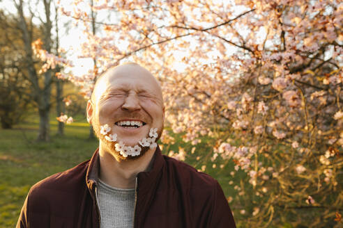 Happy man with flowers on beard near tree at park - VIVF00930