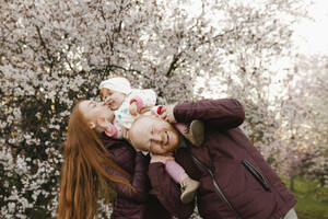 Mutter küsst Tochter, die im Park auf der Schulter des Vaters sitzt - VIVF00936
