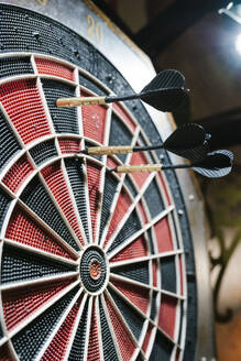 Drei schwarze Darts treffen die Dartscheibe in einer Bar - EGAF02598