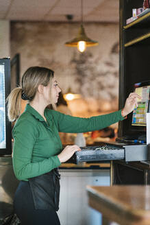 Young cashier operating touch screen computer at bar - EGAF02600