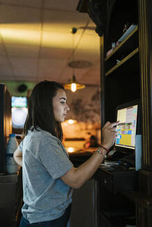 Young cashier operating touch screen computer at bar
 - EGAF02603