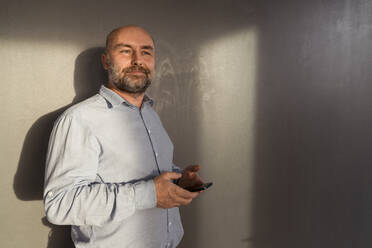 Reifer Geschäftsmann hält Mobiltelefon an eine Wand - KMKF01983