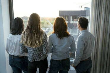 Rückansicht eines Businessteams mit Blick aus dem Fenster im Büro - KMKF02003