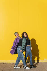 Lesbian couple posing together in front of yellow wall - MGRF00934