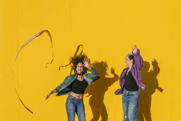Carefree lesbian couple dancing and enjoying in front of yellow wall - MGRF00952