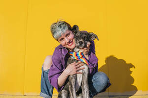 Smiling lesbian woman crouching near dog with multi colored bandana around neck - MGRF00957