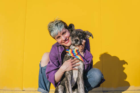 Lächelnde lesbische Frau hockt in der Nähe von Hund mit buntem Halstuch um den Hals - MGRF00957