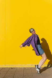 Woman with tiptoe balancing in front of yellow wall - MGRF01000