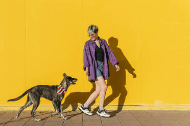Lesbian woman walking with dog in front of yellow wall - MGRF01008