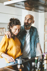 Contemplative man with arm around woman standing in kitchen at home - JOSEF19036