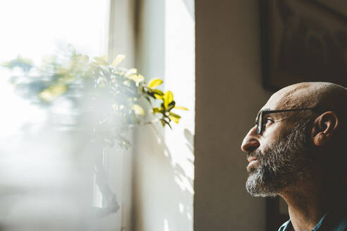 Älterer Mann mit Brille schaut zu Hause aus dem Fenster - JOSEF19059