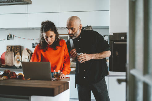 Man standing by woman using laptop in kitchen at home - JOSEF19145