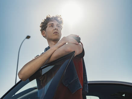 Thoughtful man leaning on car door at sunny day - MFF09312