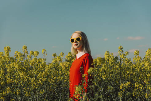 Frau mit Sonnenbrille in einem Rapsfeld stehend - VSNF00790