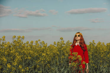 Woman wearing sunglasses standing amidst flowers in rapeseed field - VSNF00791