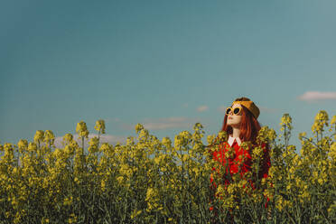 Frau mit Sonnenbrille steht in einem Rapsfeld an einem sonnigen Tag - VSNF00793