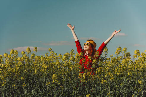Carefree woman with arms raised standing in rapeseed field - VSNF00794