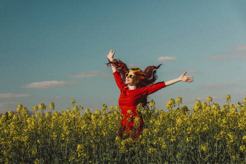 Cheerful woman enjoying with arms outstretched in rapeseed field - VSNF00795